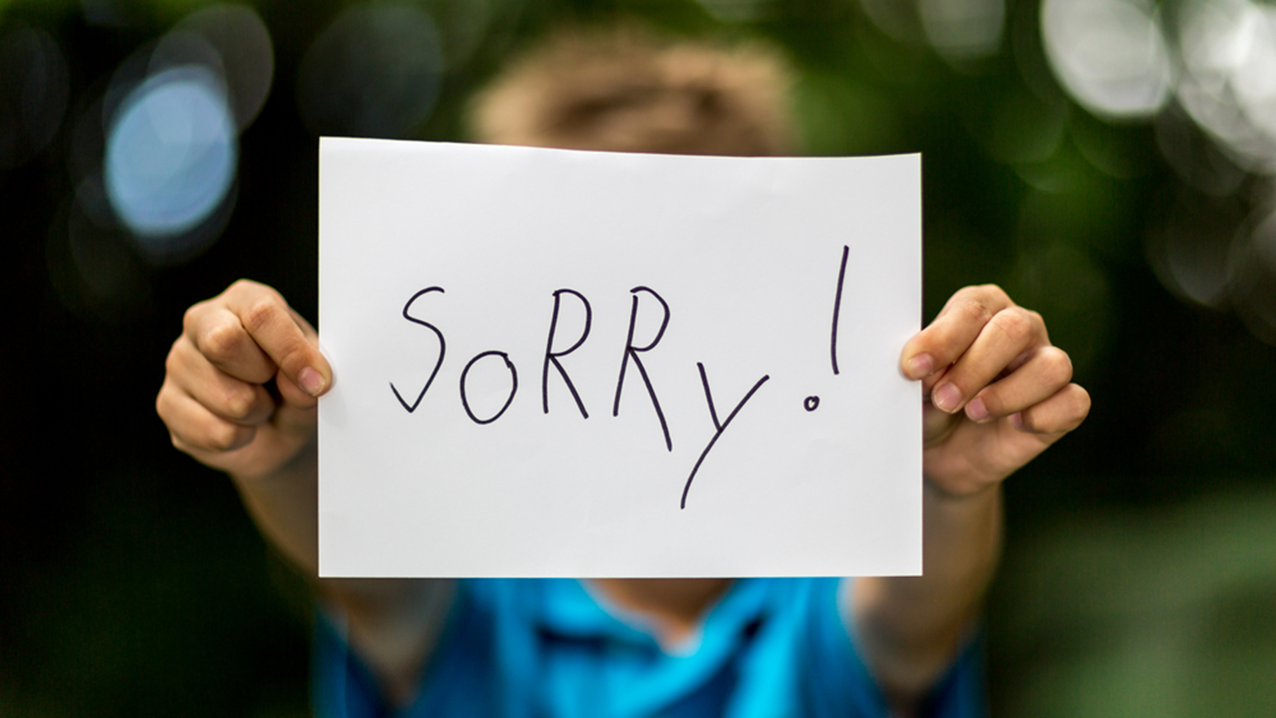 Blurred boy holding a piece of paper with the word Sorry in front of her.; Shutterstock ID 203129515; PO: Brandon for Trending